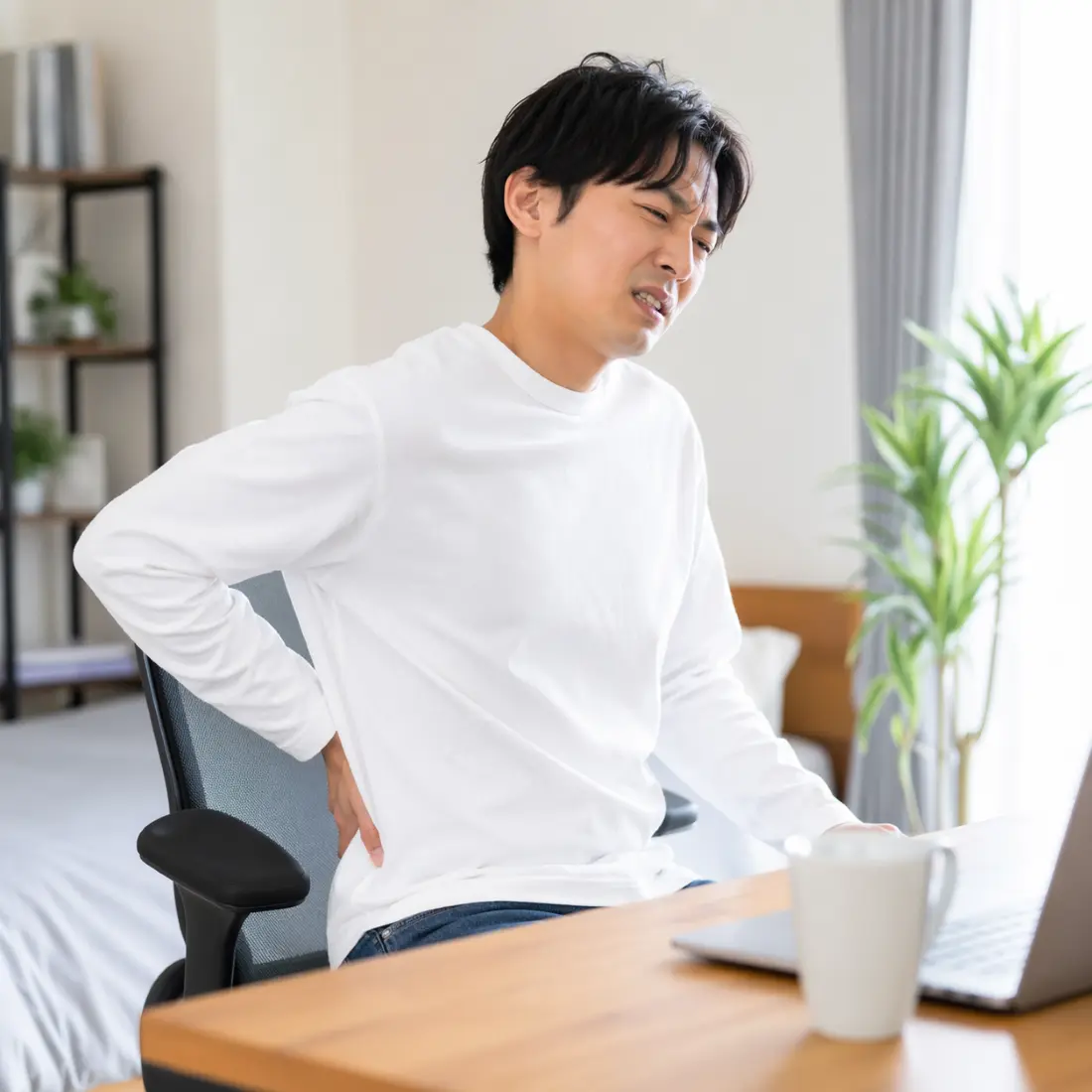 椅子に座り腰に手を当てる男性