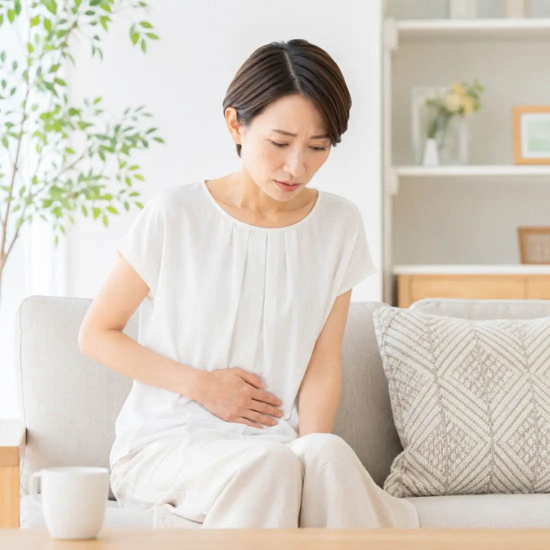 ソファーに座り下腹部に手を当てる女性
