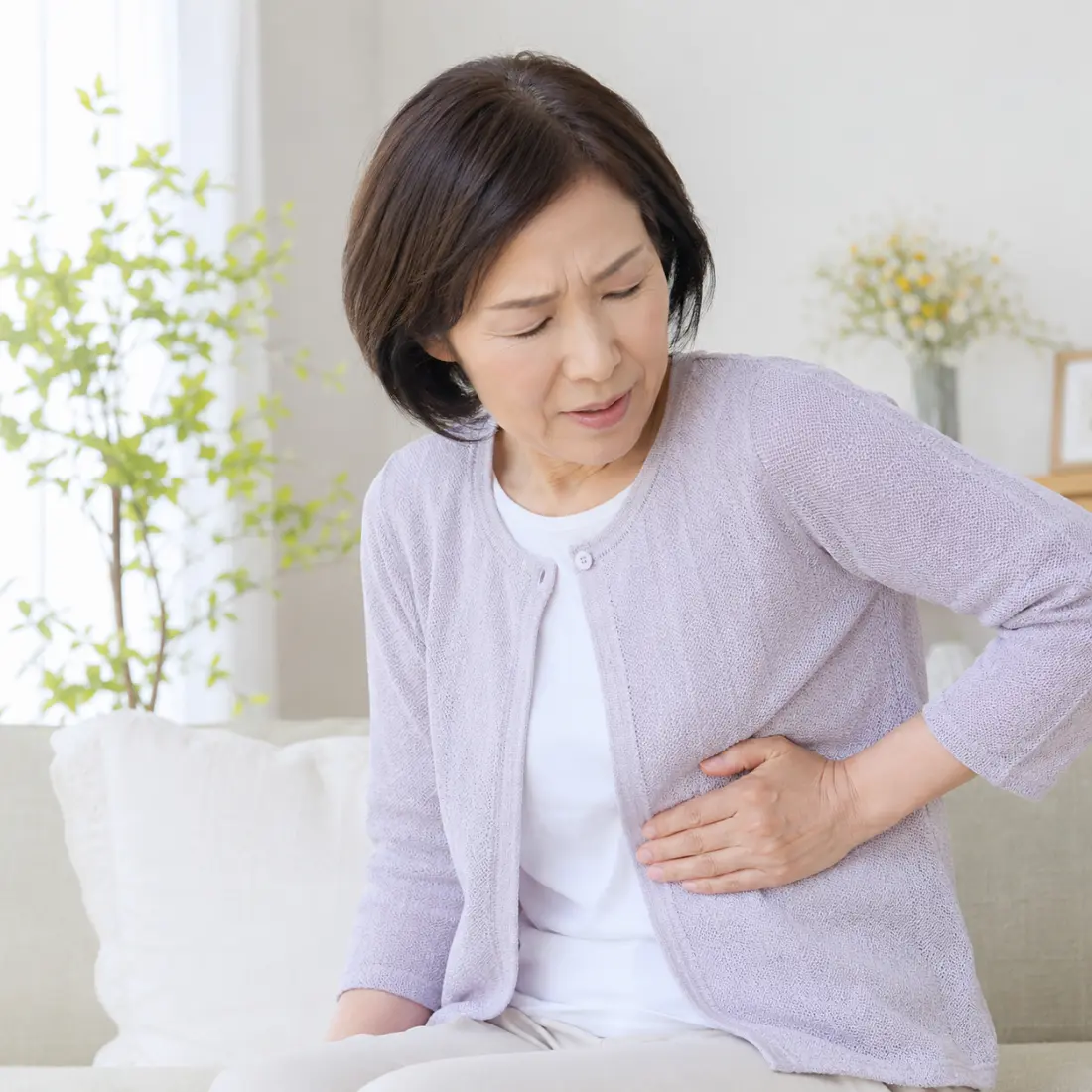 ソファーに座り脇腹に手を当てる女性