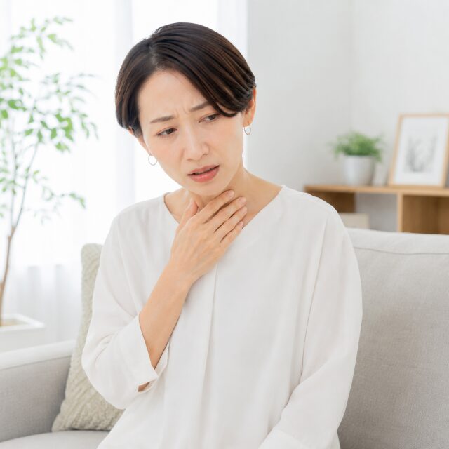 ソファーに座り喉を手で押さえている女性