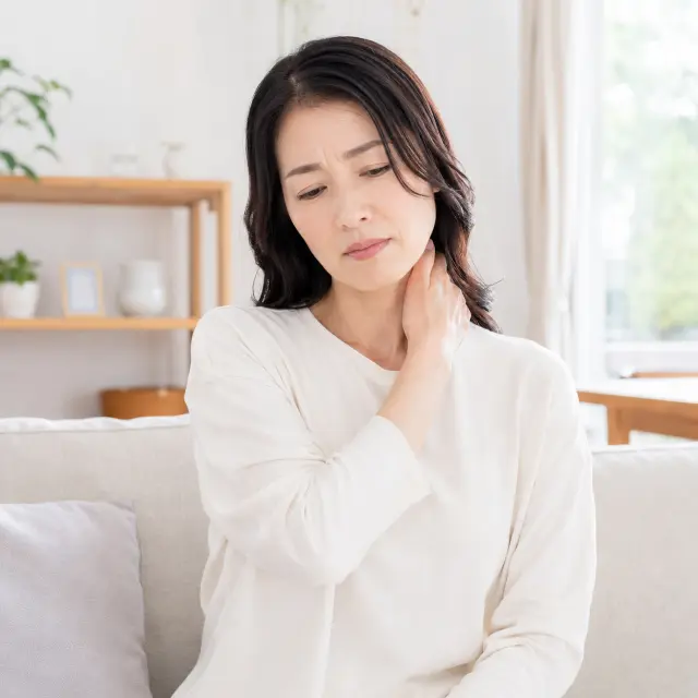 ソファーに座り首に手を当てる女性