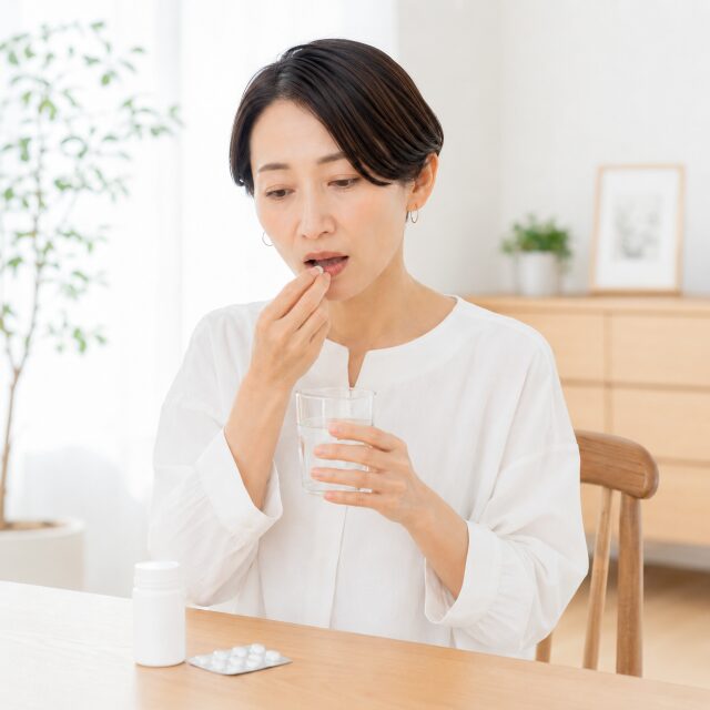 右手で薬を口に近づけ左手でコップを持つ女性