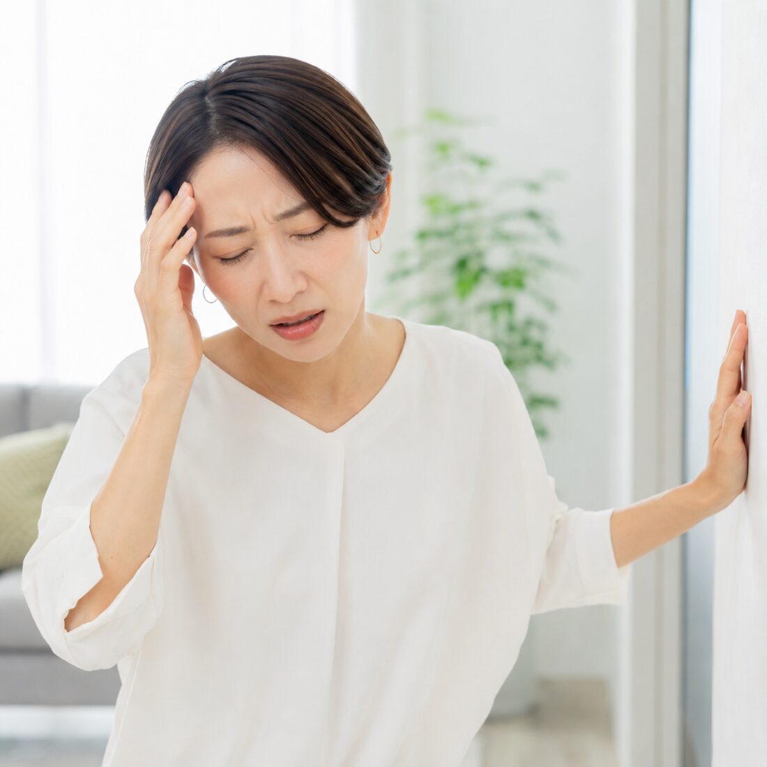 右手を額に当て、左手を壁に添えて立つ女性