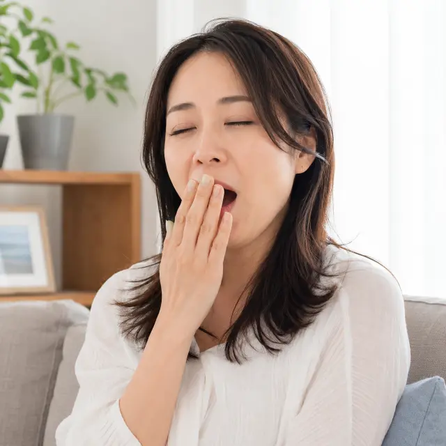口に手を当てあくびをする女性
